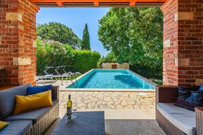 Un área de piscina con un patio de piedra, mobiliario de mimbre y una botella de vino.