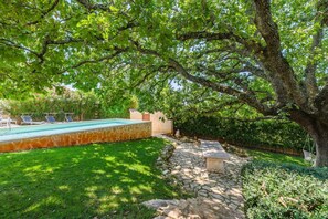 A swimming pool surrounded by a stone pathway, lush greenery, and a large tree providing shade. - Lovely Villa Near the Beach (Visnjan)
