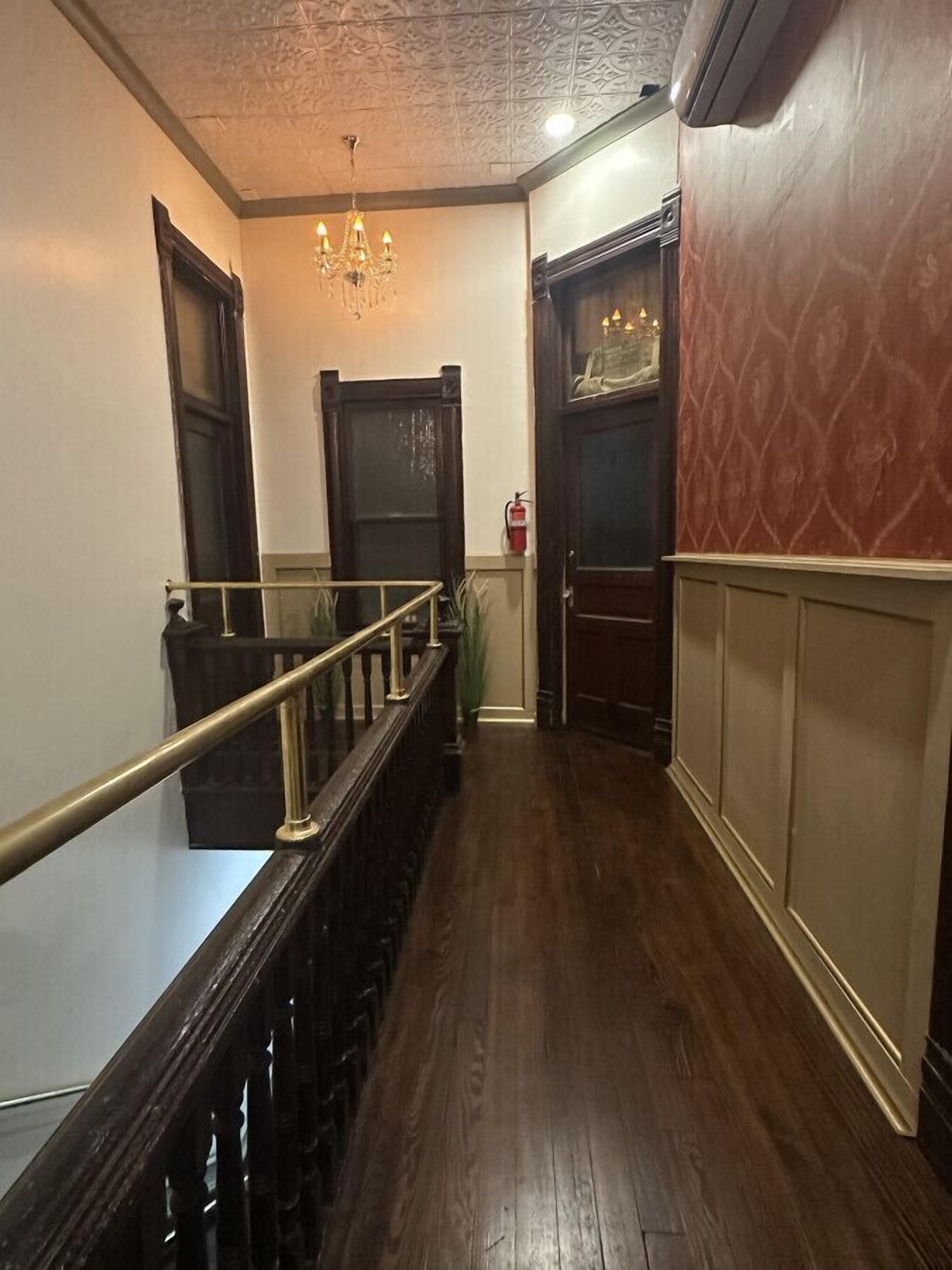 Un pasillo con una escalera de madera, un candelabro y un extintor.