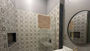 A bathroom with patterned tiles, a bathtub, a sink with gold fixtures, and a round mirror.