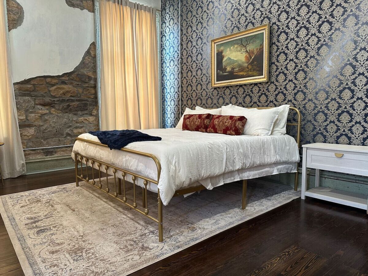 Un dormitorio con cama, mesita de noche, un cuadro en la pared y un revestimiento de pared de piedra.