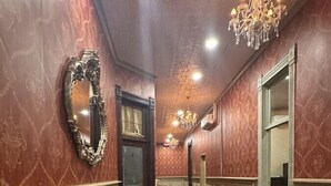 Un pasillo con suelo de madera, un candelabro, un espejo y una mesa de vidrio.