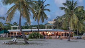 Un restaurante junto a la playa con terraza, palmeras y un edificio con techo verde.