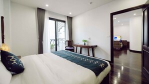 A hotel room with a large bed, a small table with a plant, a chair, and a view of the outside balcony.