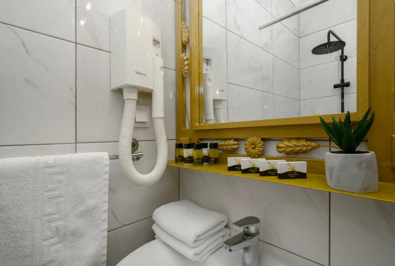A modern bathroom with a white and yellow color scheme, a hairdryer, a showerhead, a toilet, and a shelf with toiletries.