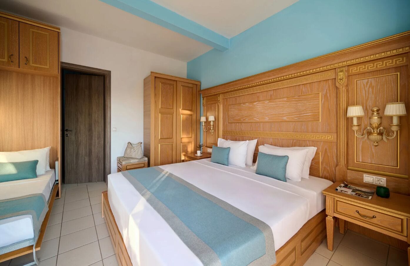 A hotel room with a large bed, wooden wardrobe, bedside tables, and a nightstand.