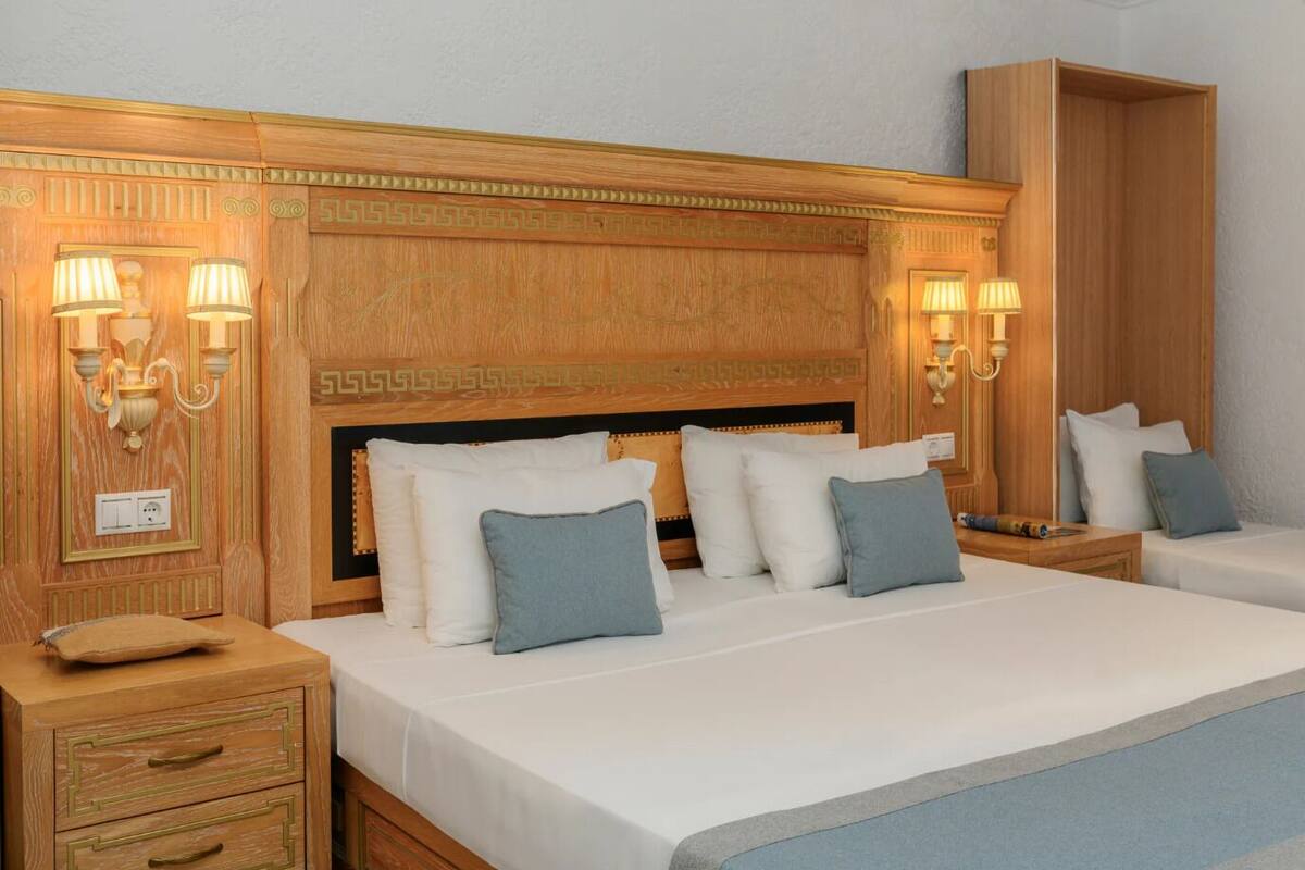 A hotel room with a large bed, two bedside tables, a nightstand, and a wardrobe.