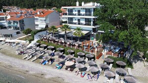 Un hôtel en bord de mer doté de nombreux balcons, d’une plage aménagée avec des parasols et des chaises longues, et offrant une vue dégagée sur la mer.