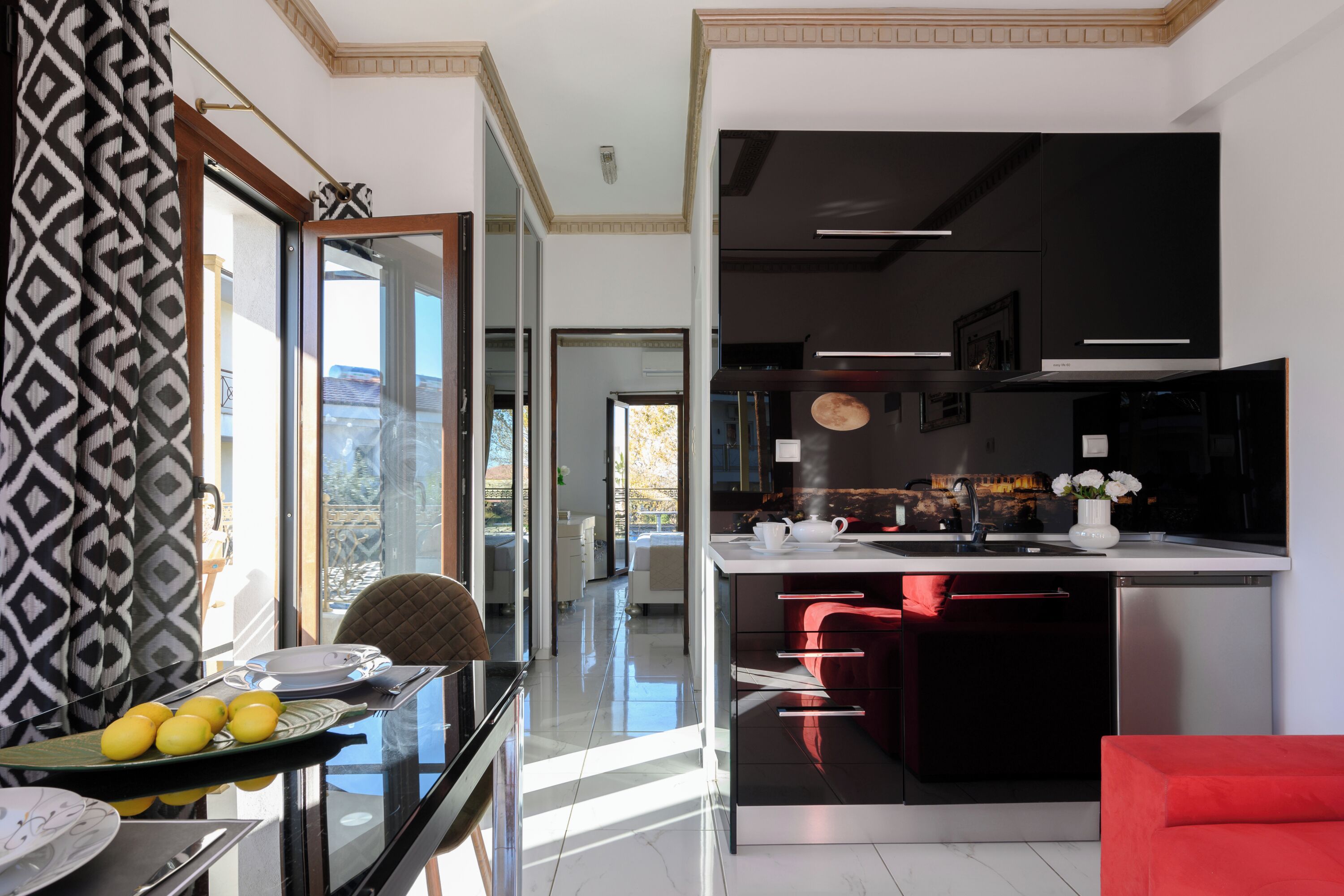 Una cocina moderna con cubierta de encimera negra, una silla roja y una zona de comedor con mesa y sillas de vidrio.