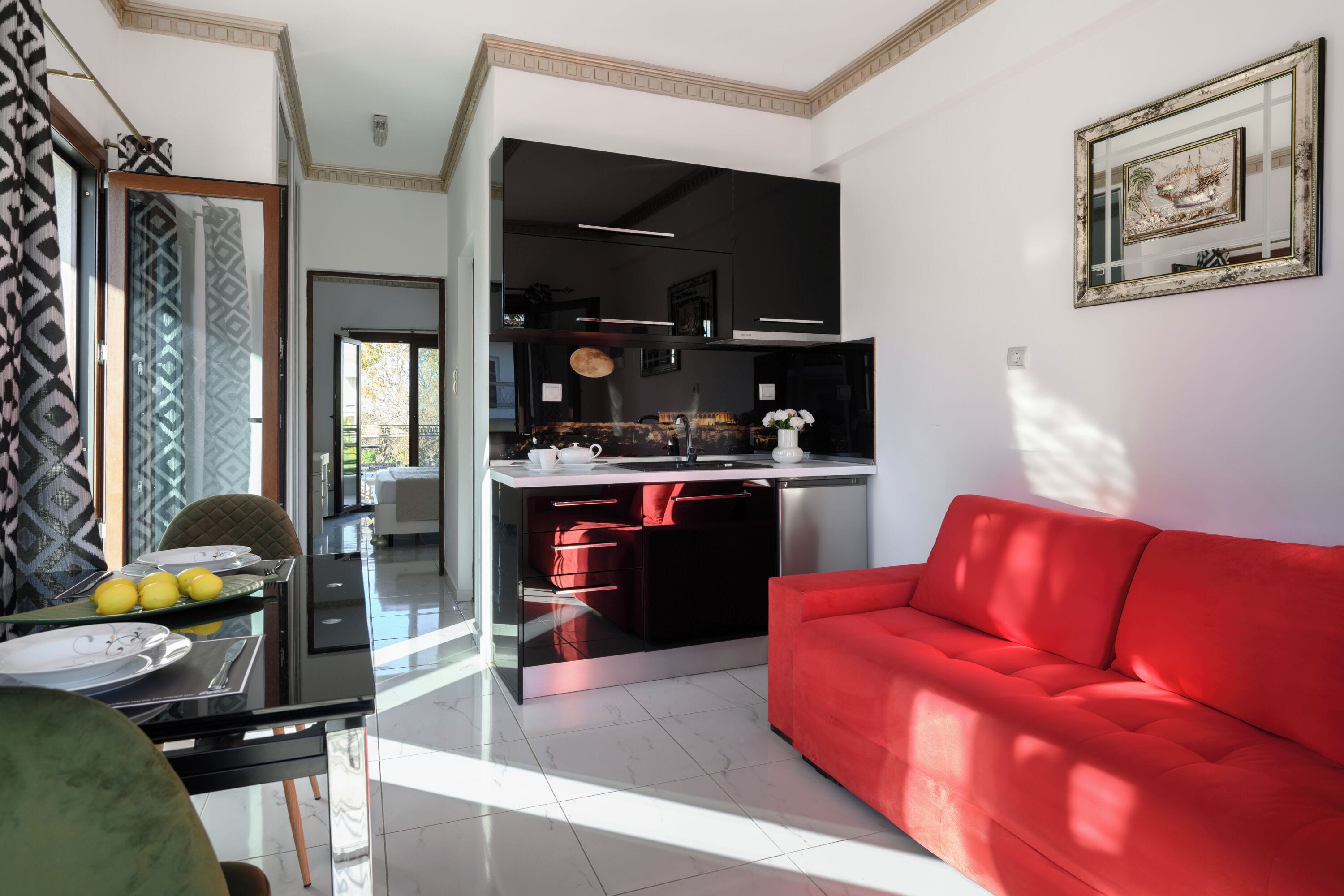 A modern kitchen with black cabinets, a red sofa, and a dining area with a glass table and chairs.