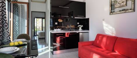 A modern kitchen with black cabinets, a red sofa, and a dining area with a glass table and chairs.