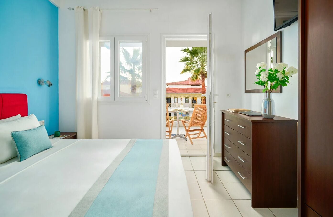 Un dormitorio con cama, cómoda, espejo y vista a un espacio exterior con mesa y sillas.
