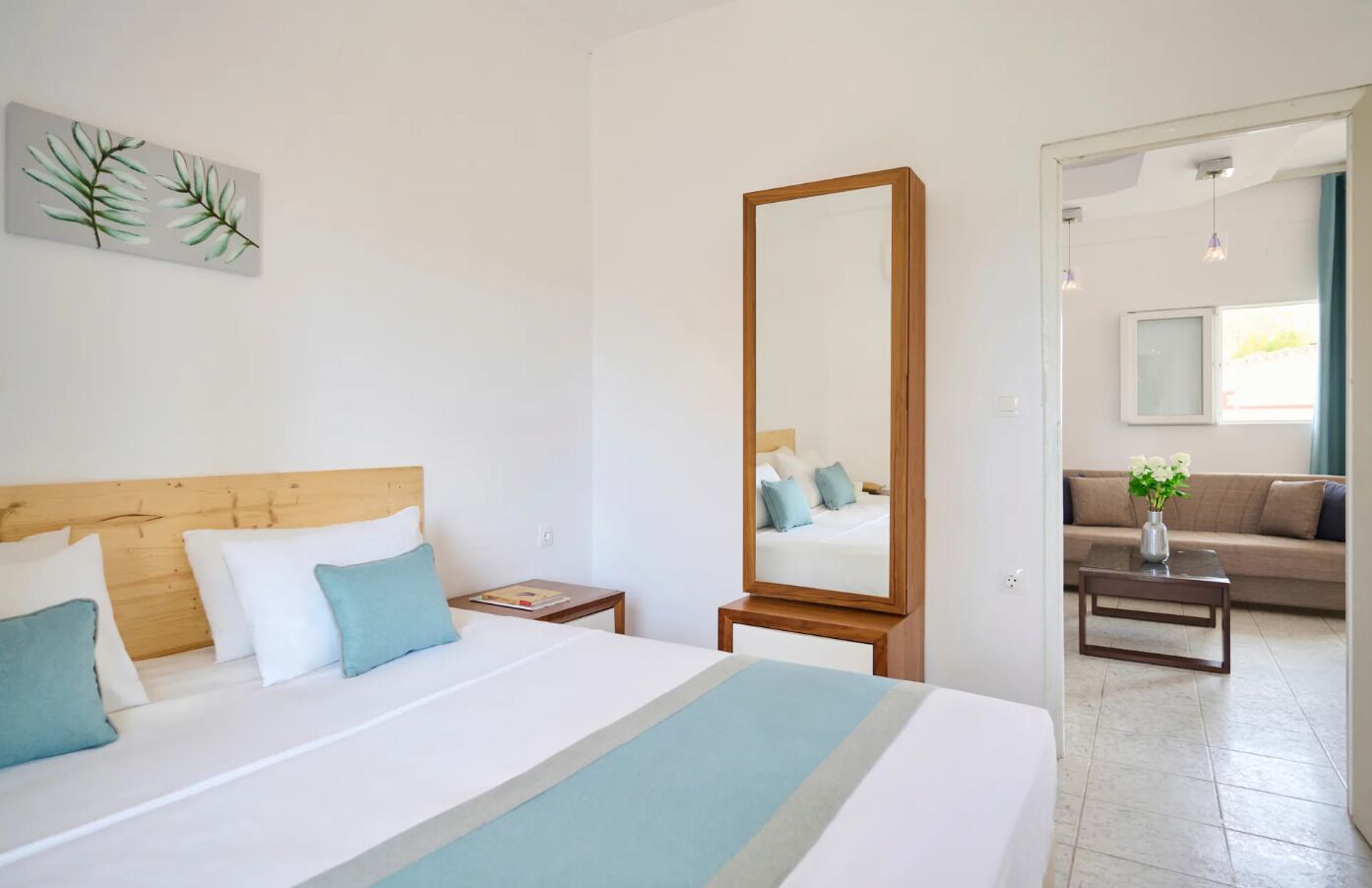 A hotel room with a large bed, a wooden headboard, a nightstand, a mirror, a sofa, and a coffee table.