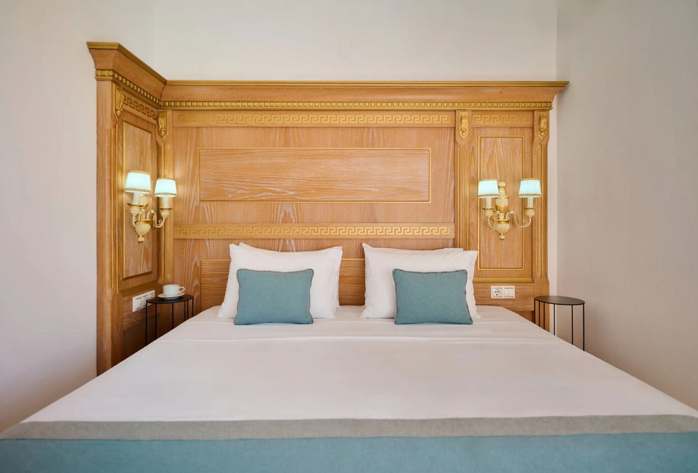 A large bed with a wooden headboard, two wall sconces, and a bedside table with a cup.