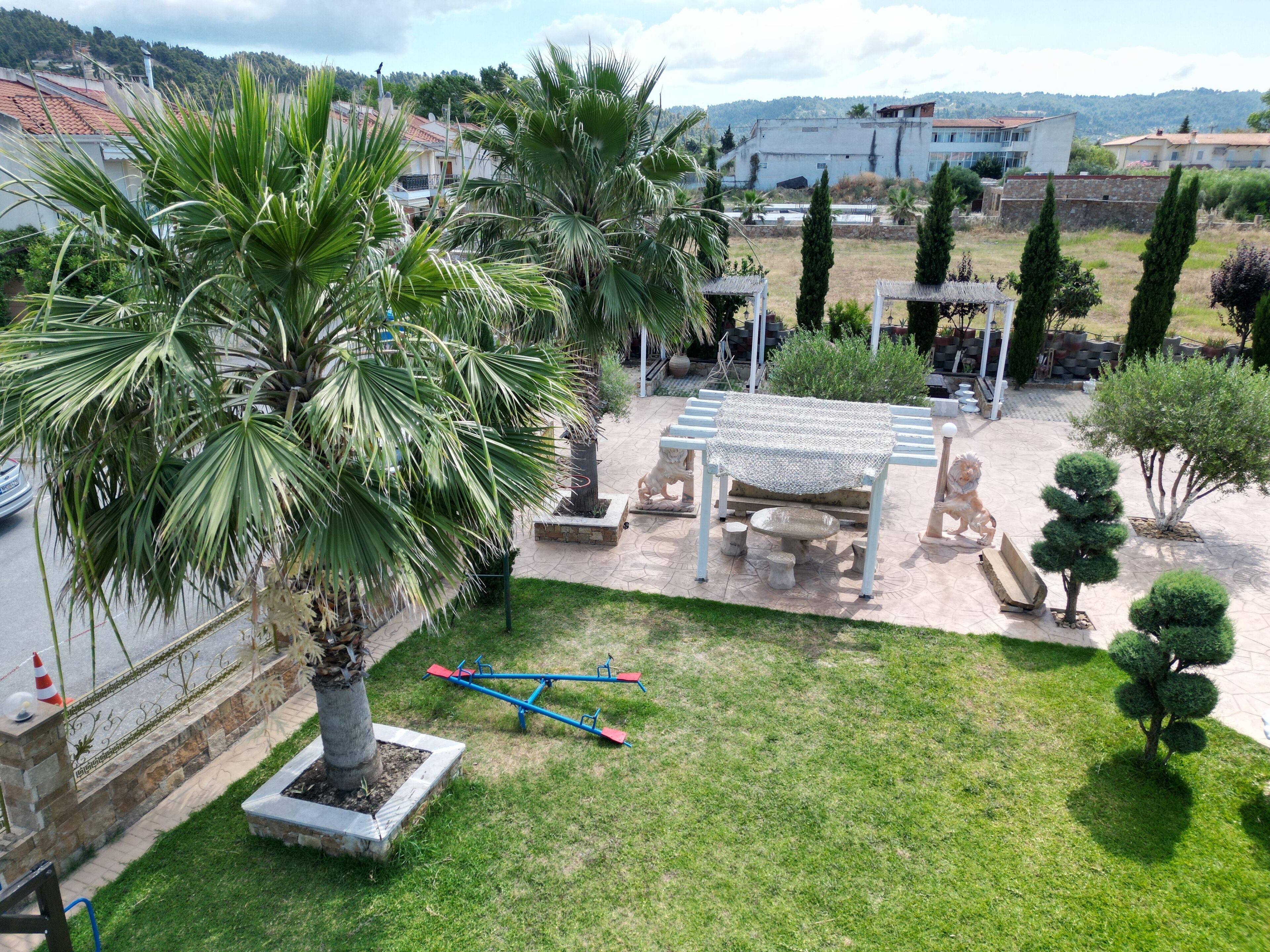 Un jardín cuidado con una palmera, un sube y baja y un pérgola con techo estampado.