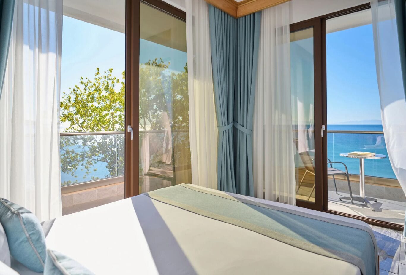 A hotel room with a bed, a balcony with a view of the sea, and a table with chairs.