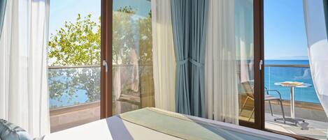 A hotel room with a bed, a balcony with a view of the sea, and a table with chairs.