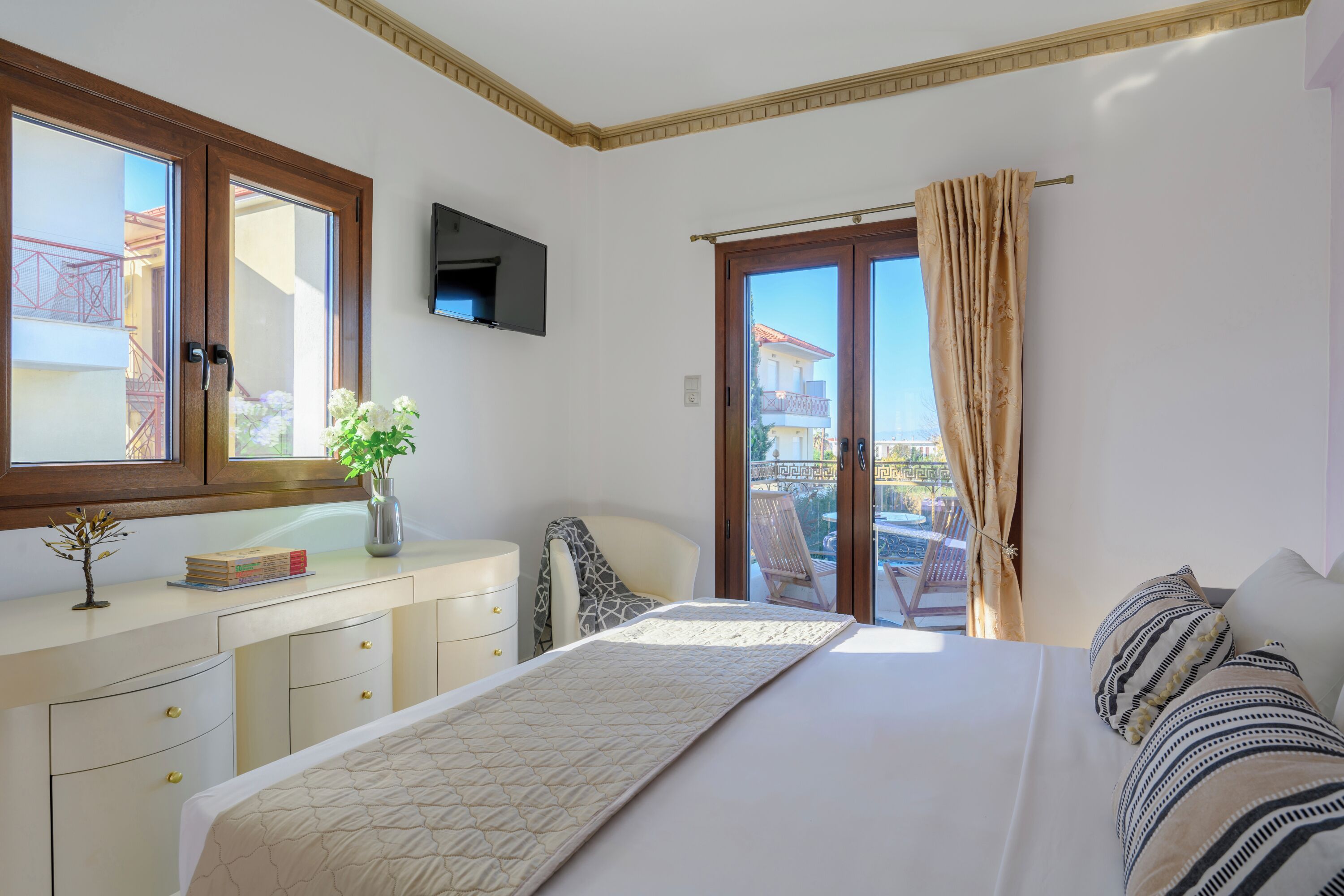A bedroom with a bed, a dresser, a TV, a window with curtains, and a view of the outside.