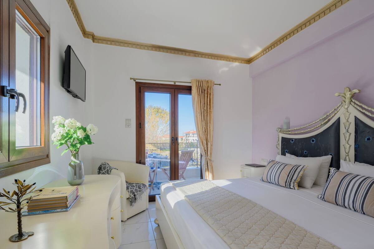 A bedroom with a large bed, a desk with a vase of flowers, a chair, and a balcony door.
