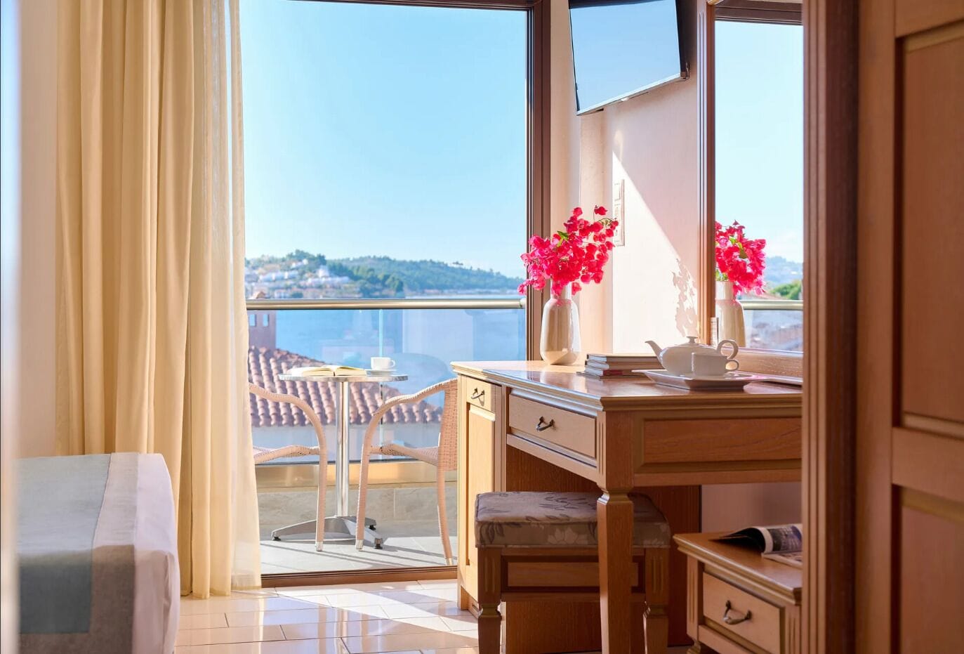 Una habitación con balcón, un escritorio con un florero y vistas a la ciudad.