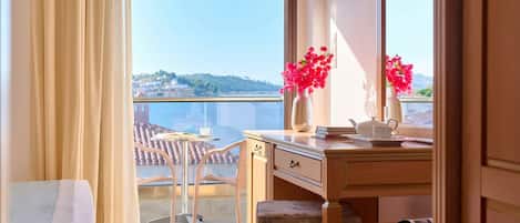 A room with a balcony, a desk with a vase of flowers, and a view of a cityscape.