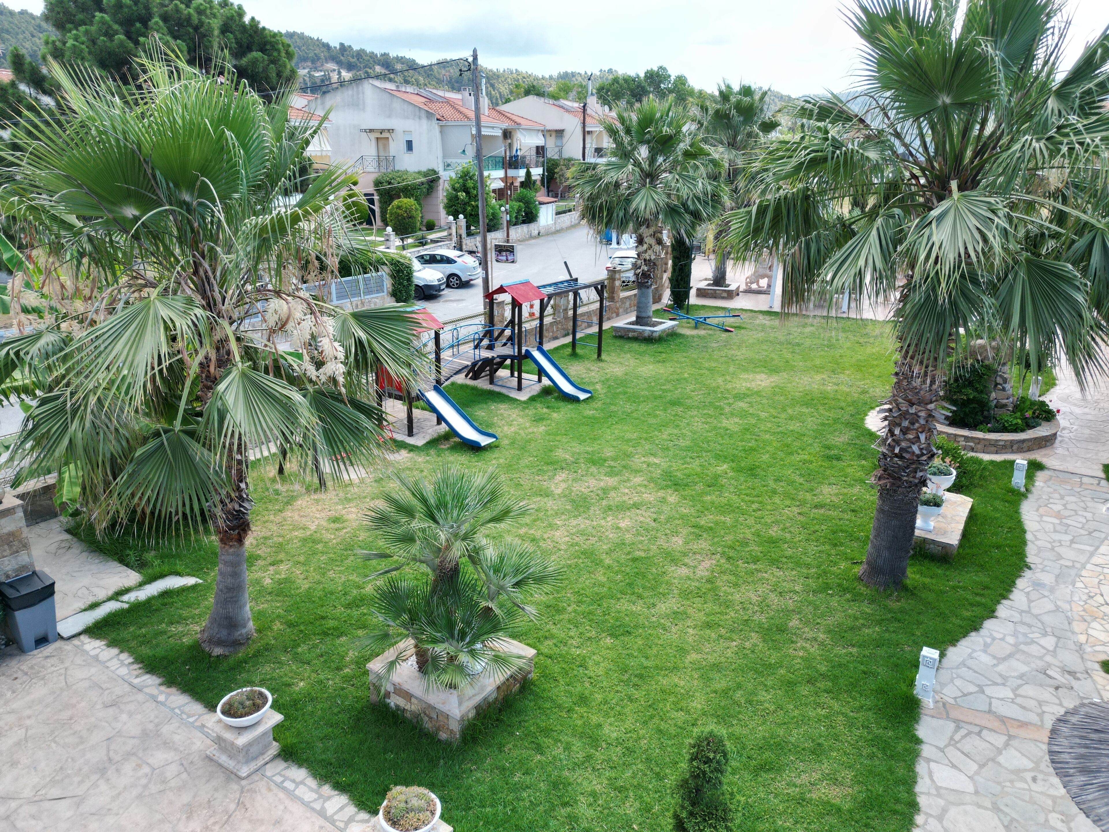 A residential area with a playground, palm trees, and a paved pathway.