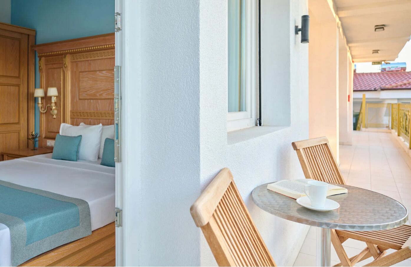 A hotel room with a bed, a small round table with a cup and saucer, and a chair.
