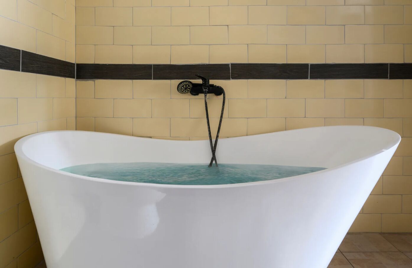 Eine freistehende Badewanne mit schwarzem Wasserhahn in einem Badezimmer mit beige- und dunkelbraunen Fliesenwänden.