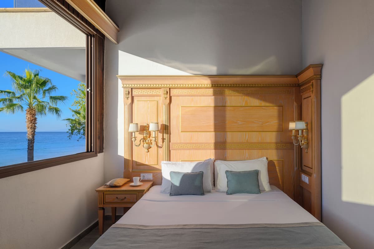 A hotel room with a large bed, a nightstand, a lamp, and a view of the ocean.