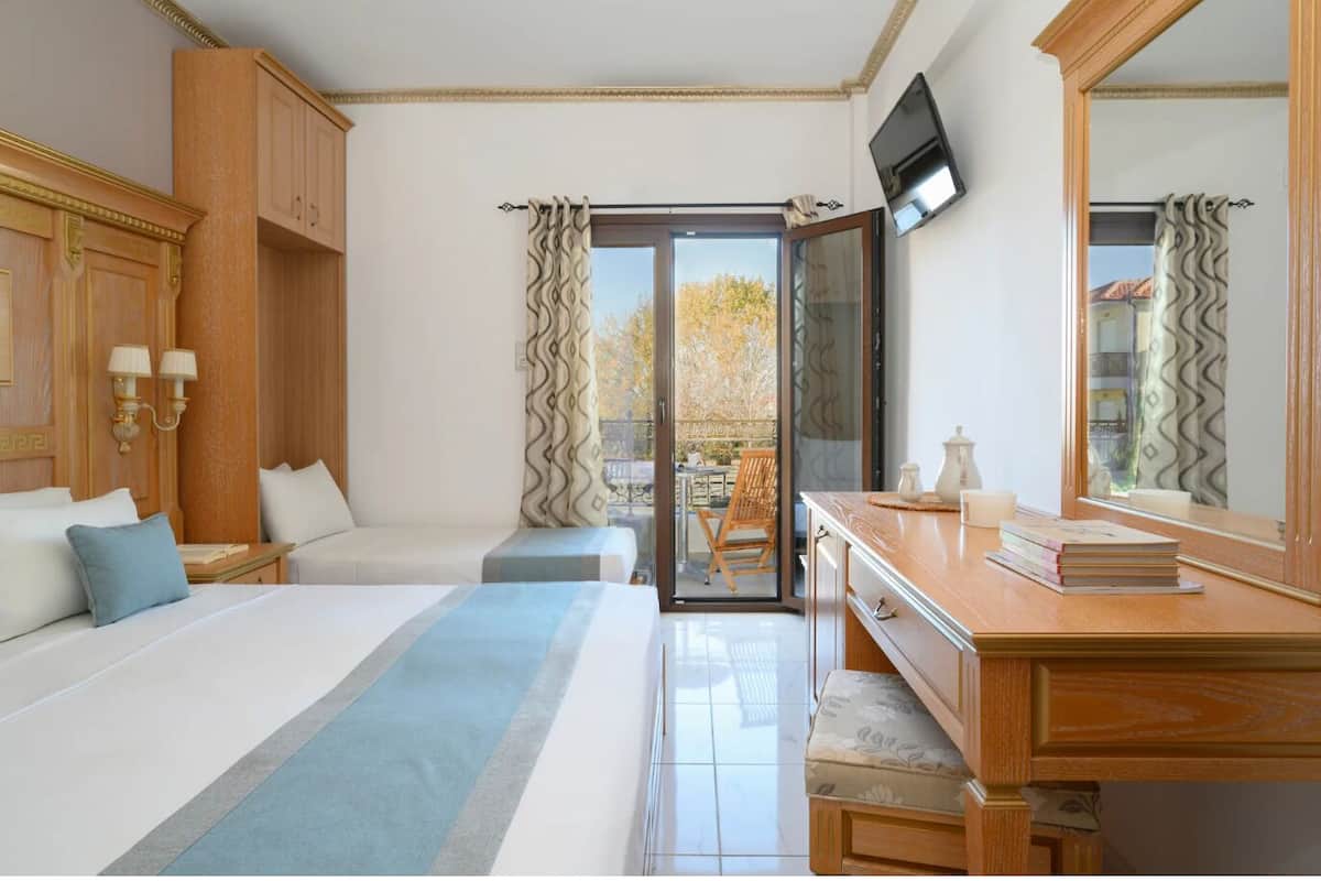 A hotel room with a bed, a desk, a chair, a TV, and a balcony with curtains.