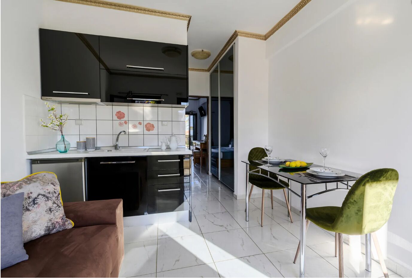 A modern kitchen with black cabinets, a white tiled backsplash, and a dining area with a table and chairs.