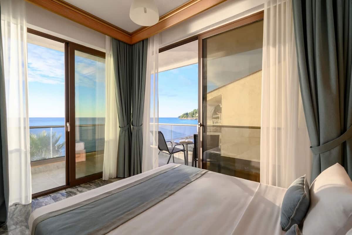 A hotel room with a large bed, a balcony with a table and chairs, and a view of the sea.