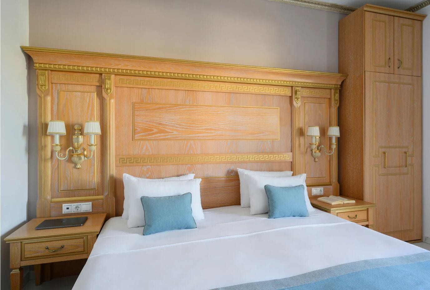A hotel room with a large bed, two bedside tables, a nightstand, and a wardrobe.