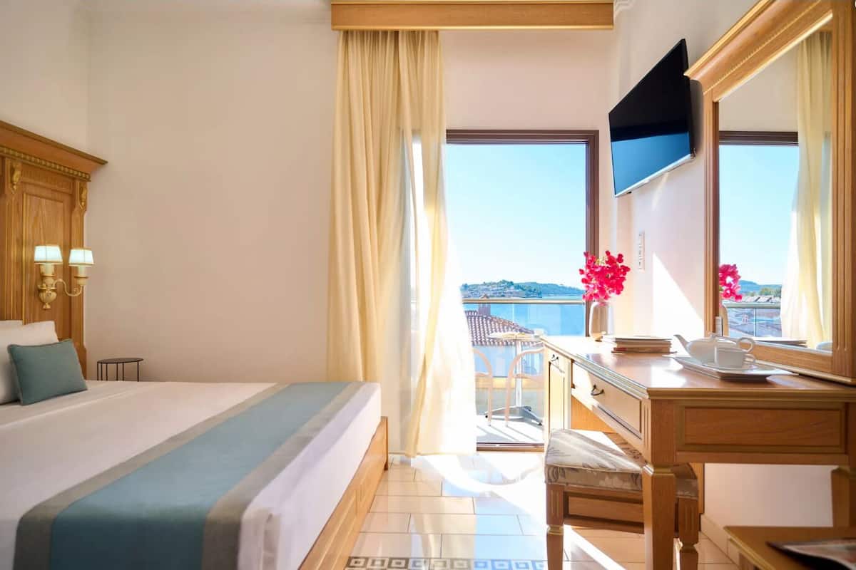 A hotel room with a bed, a desk, a TV, and a balcony with a view.