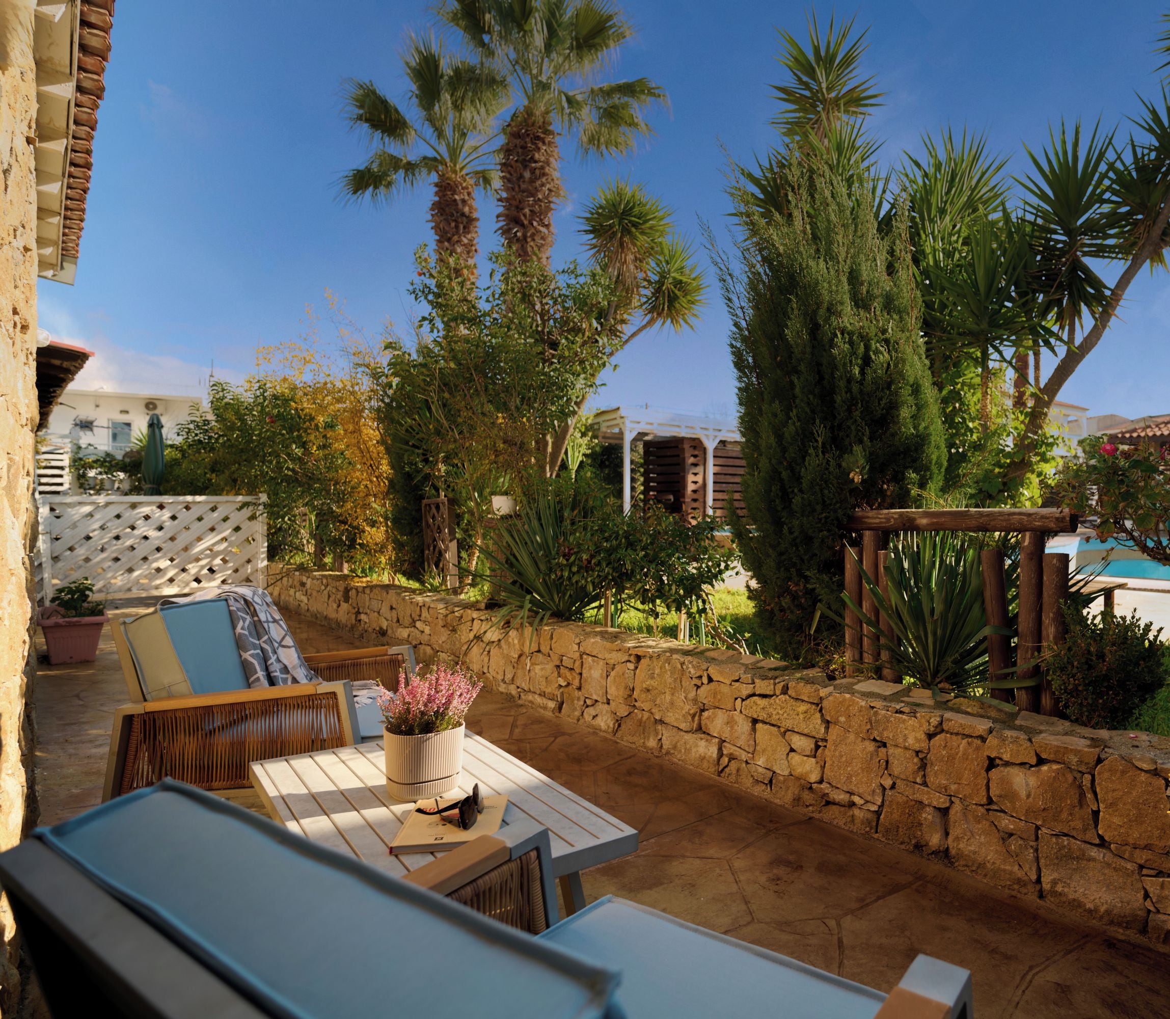 Une terrasse avec des meubles d’extérieur, un mur en pierre et une piscine en arrière-plan.