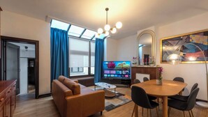 A modern living room with a sofa, a dining table with chairs, a TV, and a large window with curtains. - Fish Market Apartments (Brussels)