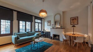 A modern living room with a sofa, coffee table, fireplace, dining table, and large windows. - Fish Market Apartments (Brussels)