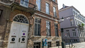 A multi-story building with a brick facade, large windows, and a white door with a circular emblem. - Fish Market Apartments (Brussels)