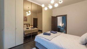 A modern bedroom with a large mirror, a bed with neatly folded towels, and a ceiling light fixture. - Fish Market Apartments (Brussels)