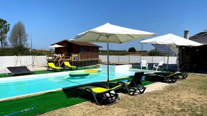 A swimming pool with lounge chairs and umbrellas, surrounded by a wooden deck and a small building.