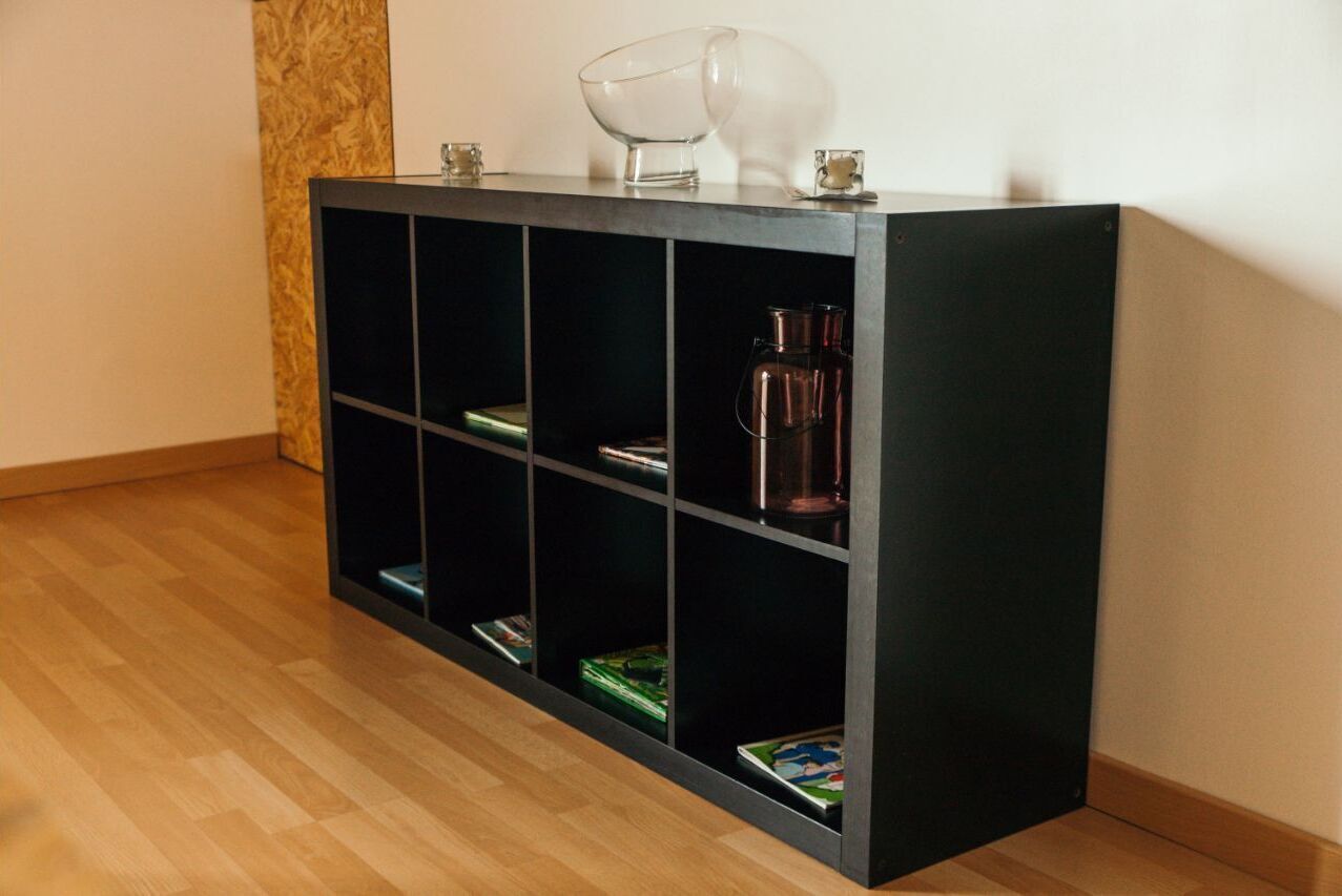Una consolle nera con diversi ripiani, alcuni dei quali contengono libri e un recipiente di vetro.