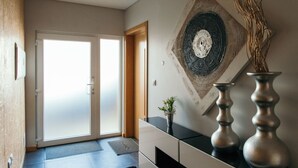 A modern interior with a sliding glass door leading to a bright room, a decorative wall piece, and two metal vases on a console table.