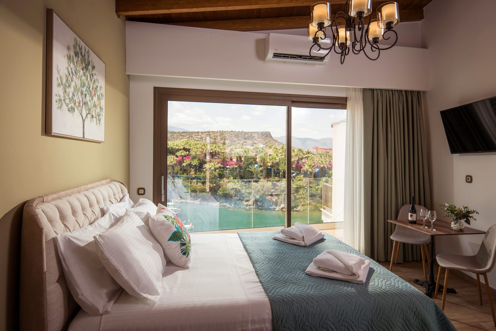 Quarto de hotel com cama, escrivaninha, cadeira, televisão e uma grande janela com vista para uma piscina e áreas verdes.