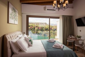 A hotel room with a bed, a desk, a chair, a TV, and a large window with a view of a pool and greenery.