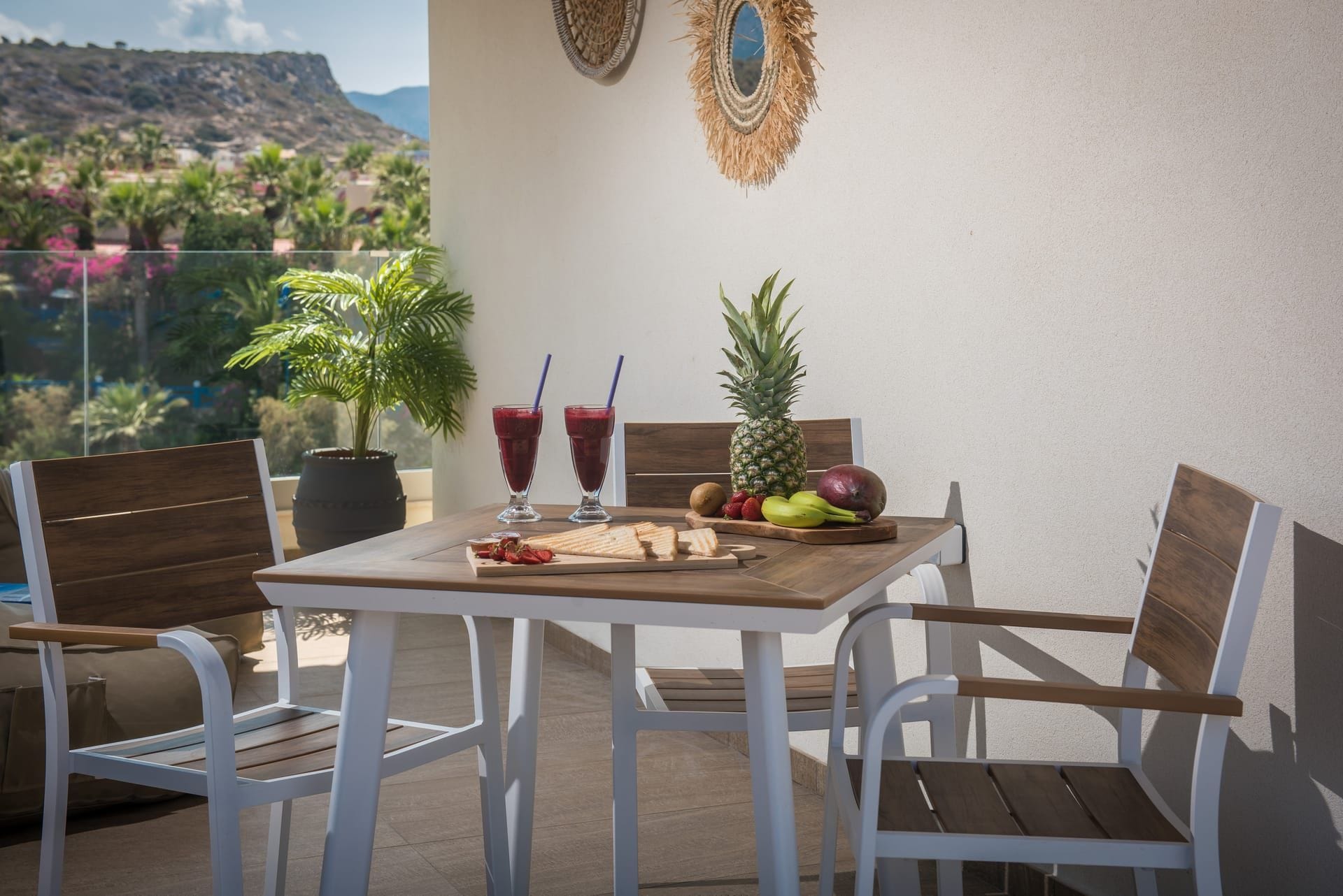 Ein Balkon mit einem Tisch für zwei Personen, mit Ananas, Kiwi, Erdbeeren und einem Schneidebrett mit Brot.