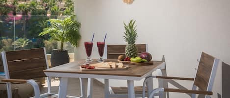 En balkong med ett bord dukat för två personer, med en ananas, kiwi, jordgubbar och en skärbräda med uppskivad bröd.
