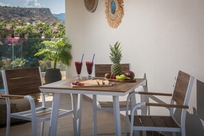 A balcony with a table set for two, featuring a pineapple, kiwi, strawberries, and a cutting board with sliced bread.