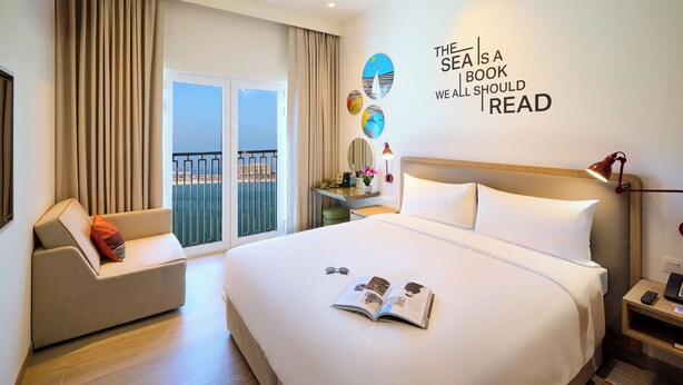 Une chambre d’hôtel dotée d’un grand lit, d’un coin lecture avec un canapé, d’un bureau et offrant une vue sur la ville depuis le balcon.