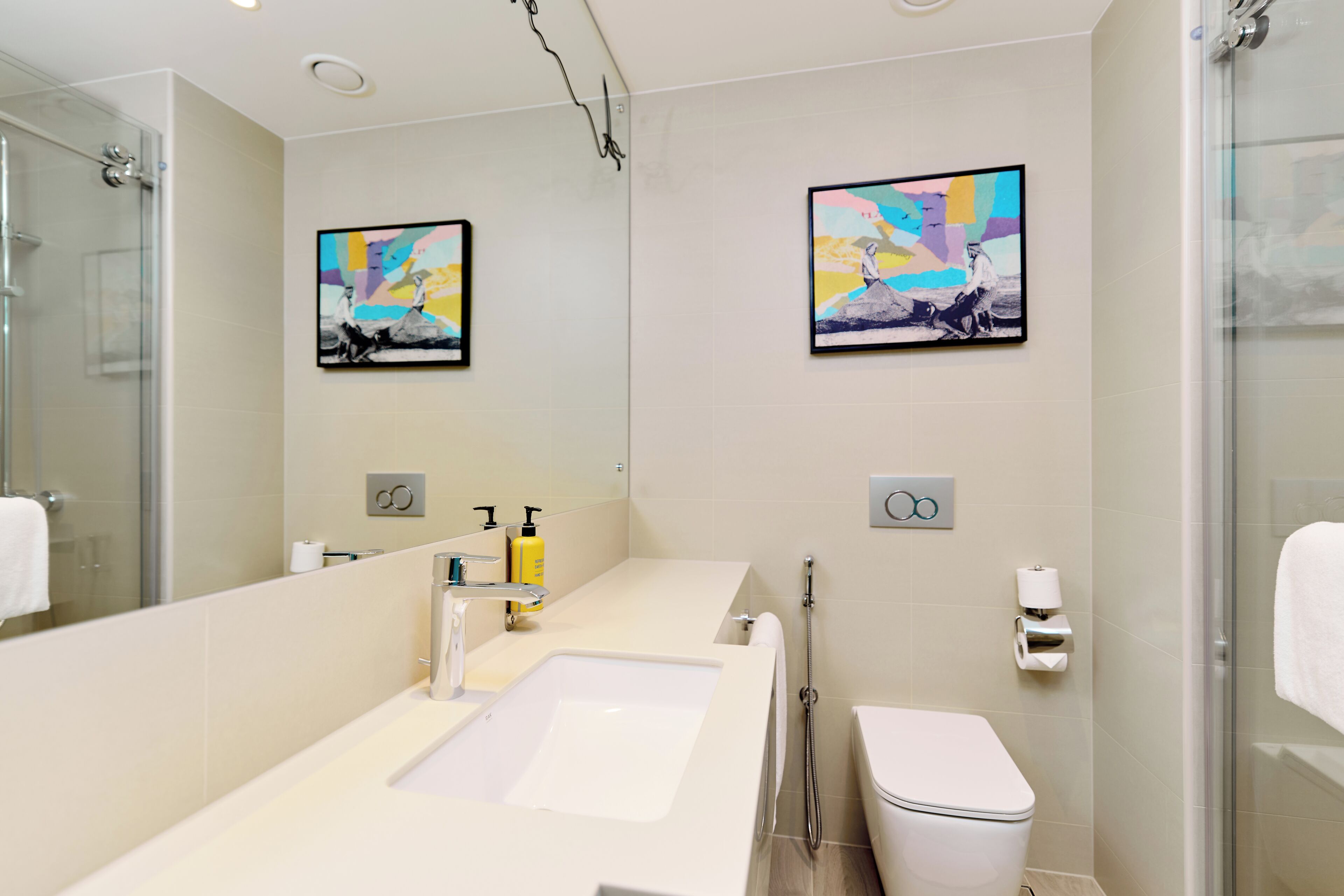 Un baño moderno con un espejo grande, un lavamanos, un inodoro y dos obras de arte enmarcadas en la pared.