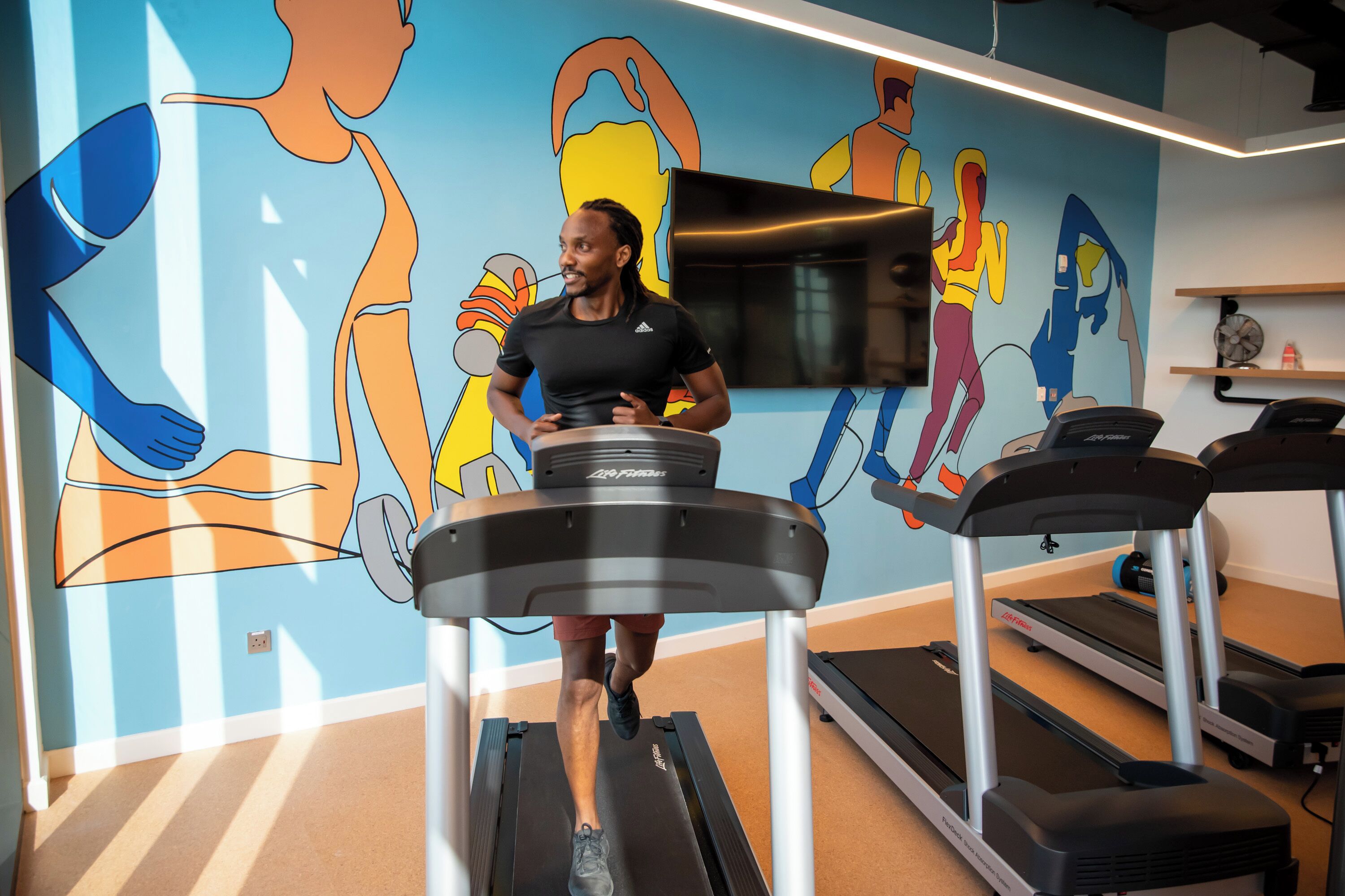A person running on a treadmill in a room with a colorful mural on the wall.